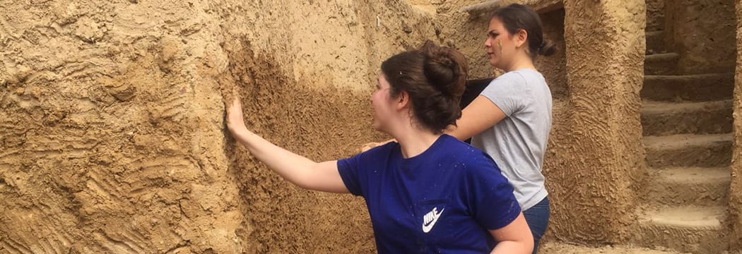 Design students study an earthen wall during fieldwork.